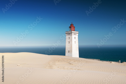 Bright beach sand dunes with the famous danish landmark lighthouse with blue sky background. Rubjerg Knude Lighthouse, Lønstrup in North Jutland in Denmark, Skagerrak, North Sea
