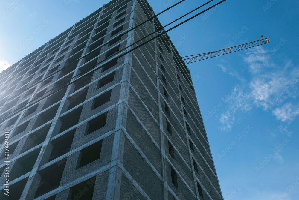 Obraz premium Multi-storey under construction building and construction crane on clear sky background.
