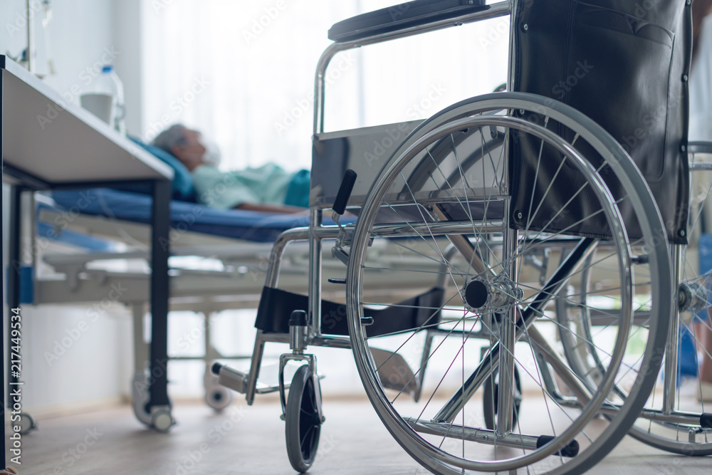 old asian senior disable laydown on bed with foreground of wheelchair in hospital