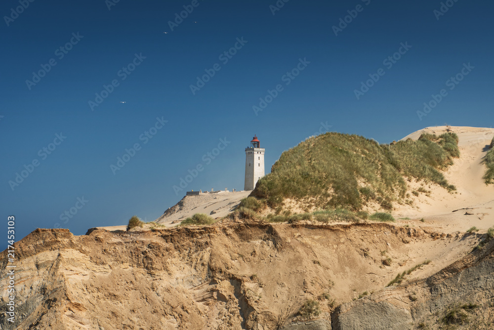 Beautiful cliff beach sand dunes and landmark lighthouse landscape scene with blue sky. Rubjerg Knude Lighthouse, Lønstrup in North Jutland in Denmark, Skagerrak, North Sea