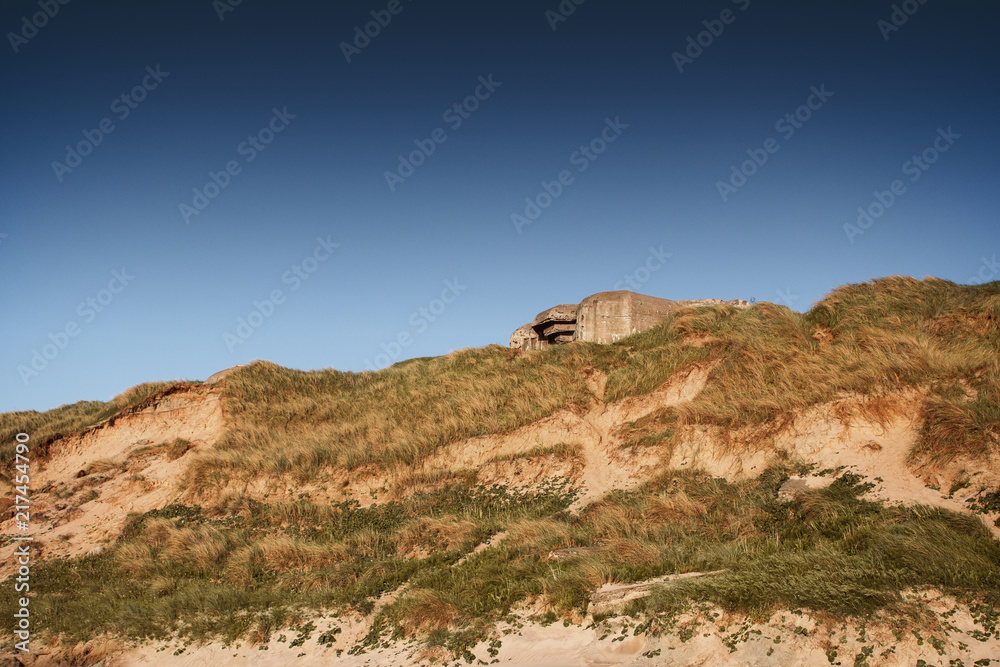Concrete Bunker from the atlantic wall in grass sand dunes at moody sunset light. Danish Coastline. Lonstrup in North Jutland in Denmark, Skagerrak, North Sea Concrete Bunker from the atlantic wall in grass sand dunes at moody sunset light. Danish Coastline. Lonstrup in North Jutland in Denmark, Skagerrak, North Sea