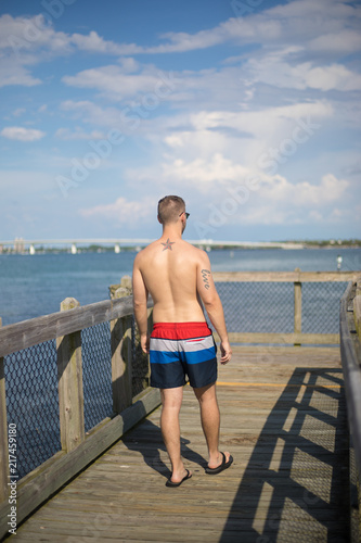 Young White Man Walking Down Florida Pier in Swim Trunks