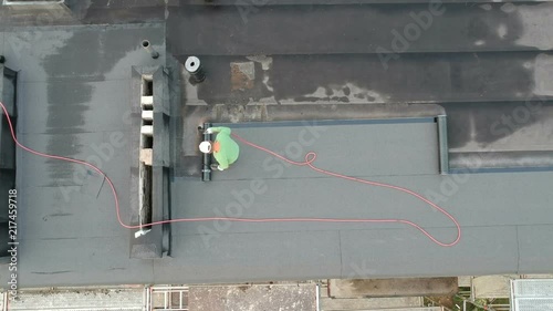 Worker on flat roof fixing waterproofing material, aerial view

