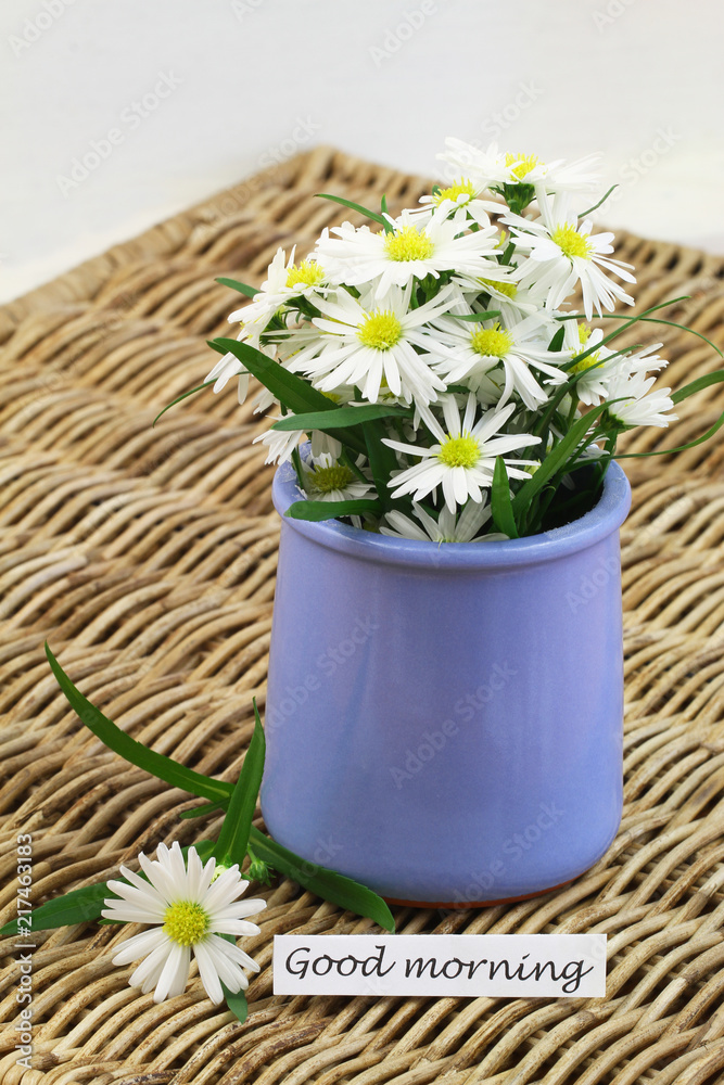 Good morning card with white daisies in blue vase on wicker surface

