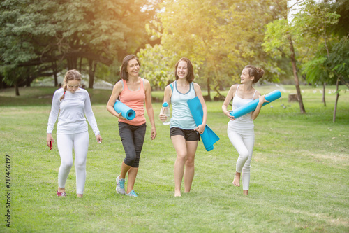 Sporty women with yoga mats talking and laughing to each other after exercising in the park