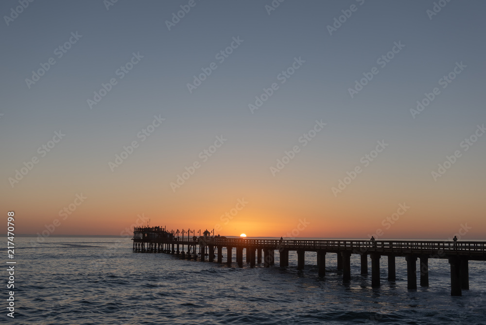Long pier above ocean waves at sunset with sun in center, Africa