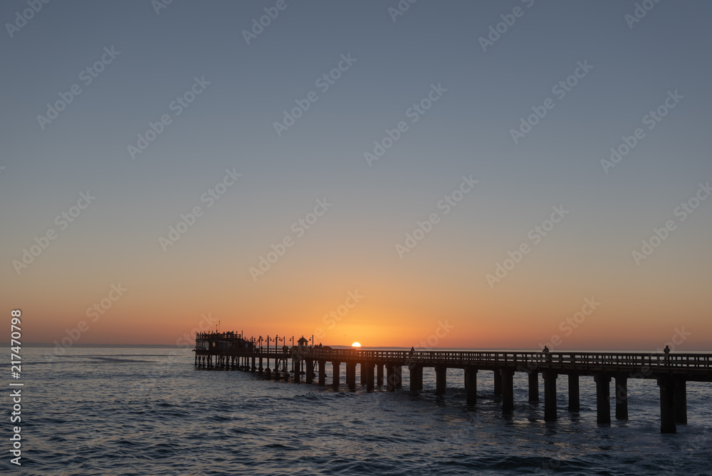 Long pier above ocean waves at sunset with sun in center, Africa Long pier above ocean waves at sunset with sun in center, Africa