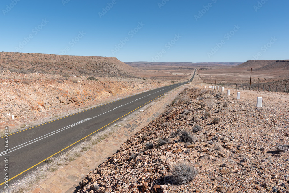 Endless straight road though dry region, horizon with blue sky