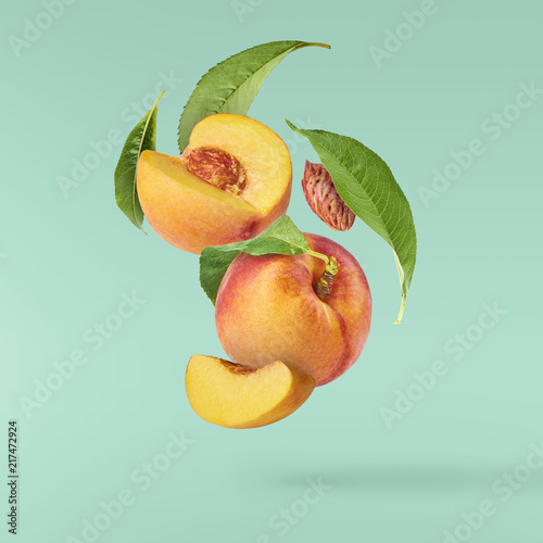 Fototapete Flying fresh ripe peach with green leaves isolated