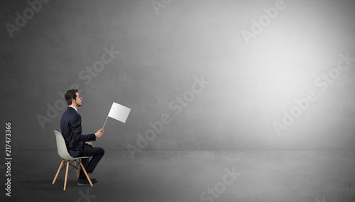 Photos Businessman staying in an empty grey dark room with stuffs on his lap