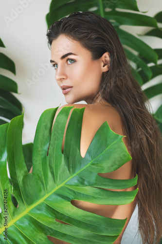 Portrait of young and beautiful woman with perfect smooth skin in tropical leaves