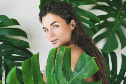 Portrait of young and beautiful woman with perfect smooth skin in tropical leaves