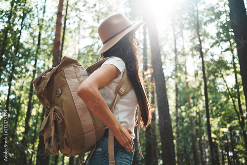 Bareve handsome woman wearing treaveler backpack and hat stand among trees on outdoors photo