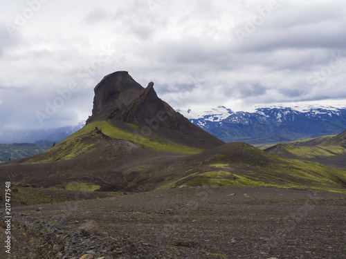 volcanic landscape in Nature reserve Fjallabak in central Iceland with mountain einhyrningur with green moss and blue snow covered mountain range, moody sky background