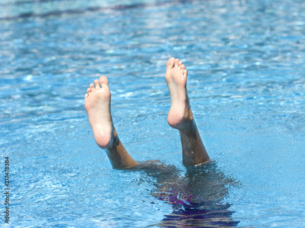 Legs of a girl diving into the water, sticking out of the pool
