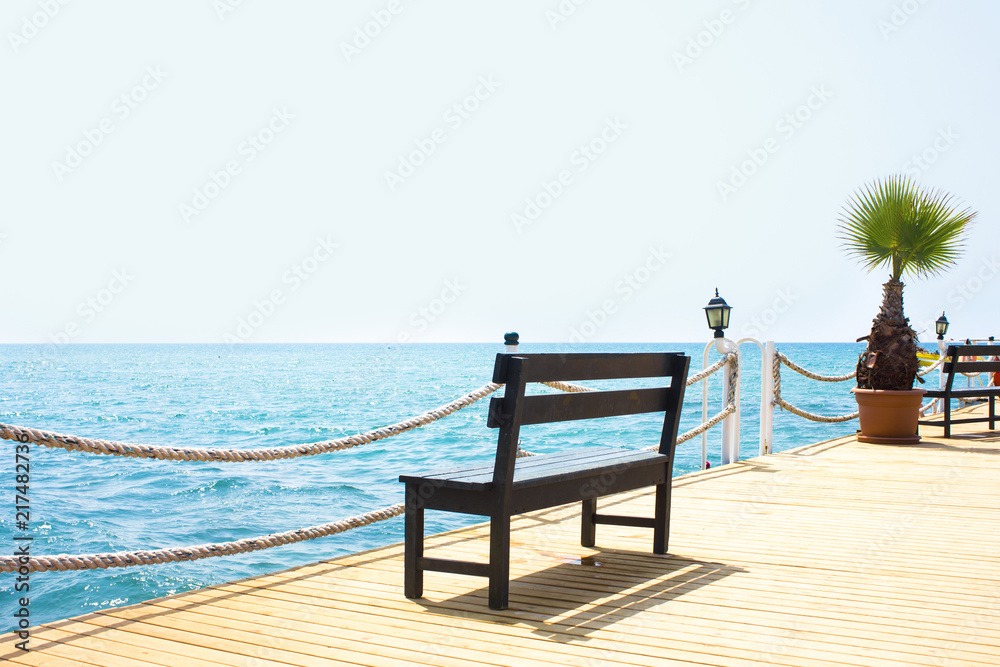 Wooden bench on the pier by the sea with a boat