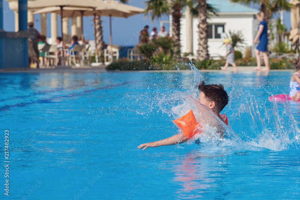 European boy in floating sleeves jumping into swimming pool.