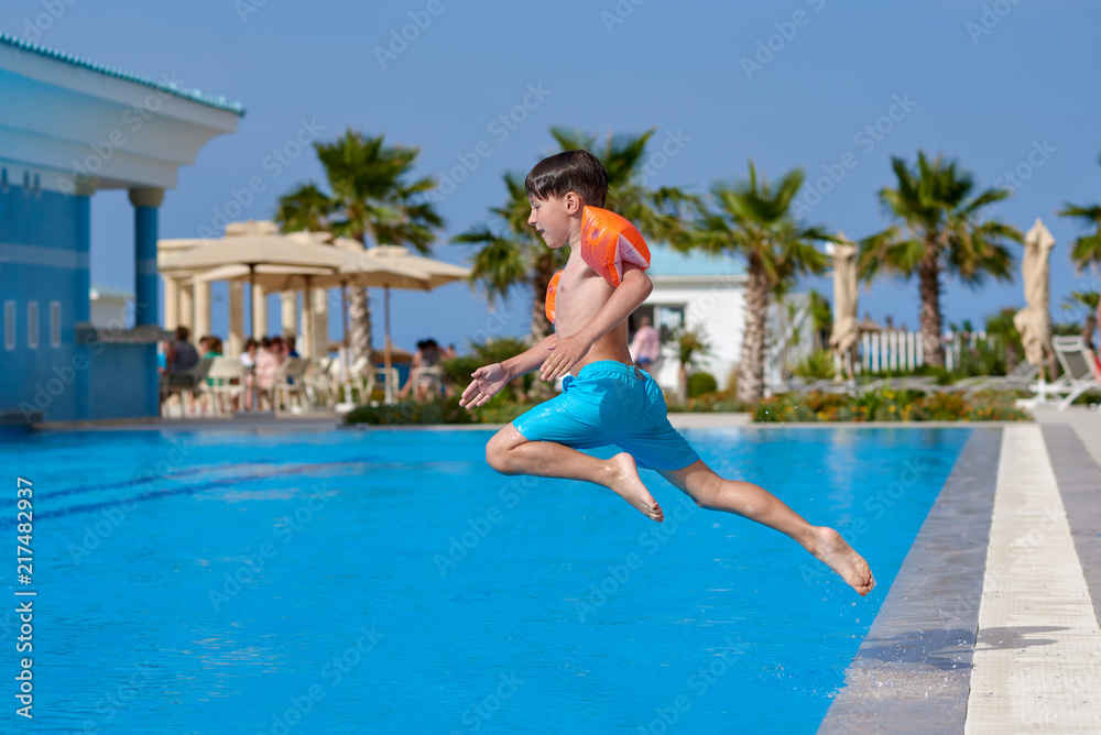 Caucasian boy having fun jumping into swimming pool at resort.