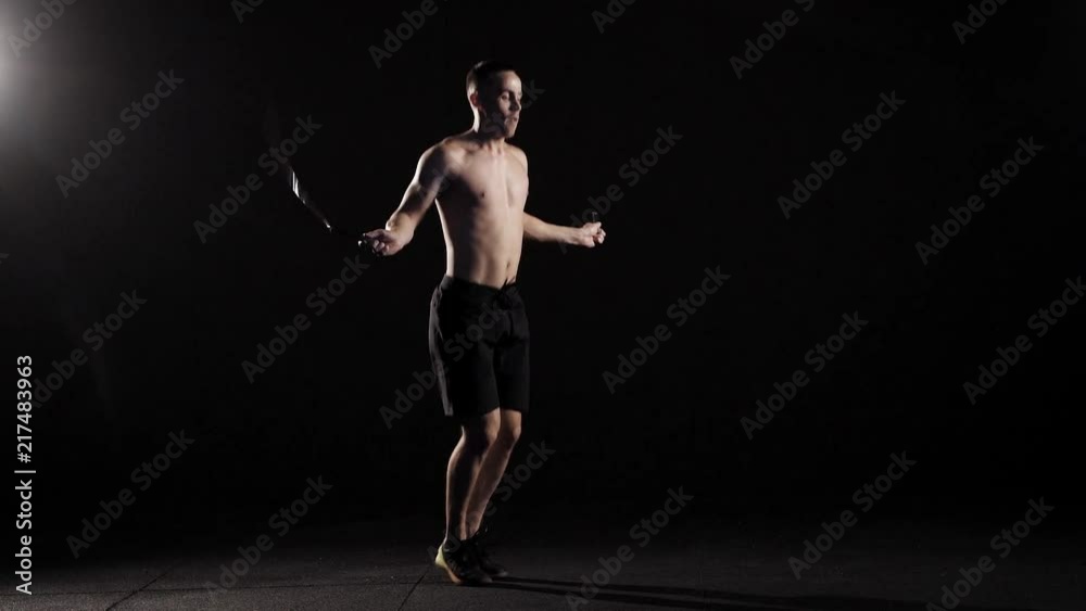 Muscular man skipping rope in a dark studio. Muscular man skipping rope in a dark studio.