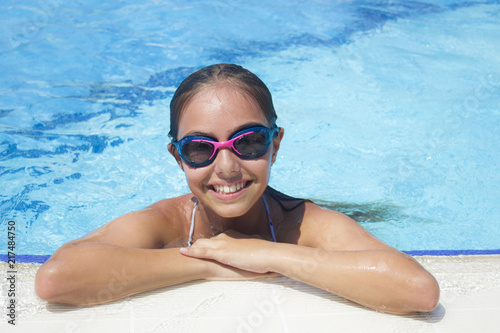 Beautiful teen girl in the pool looks at the camera from the water