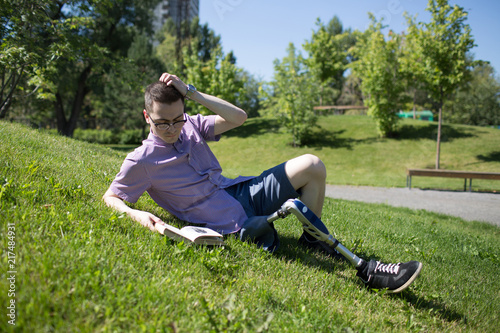 Disabled young man with foot prosthesis read book on grass