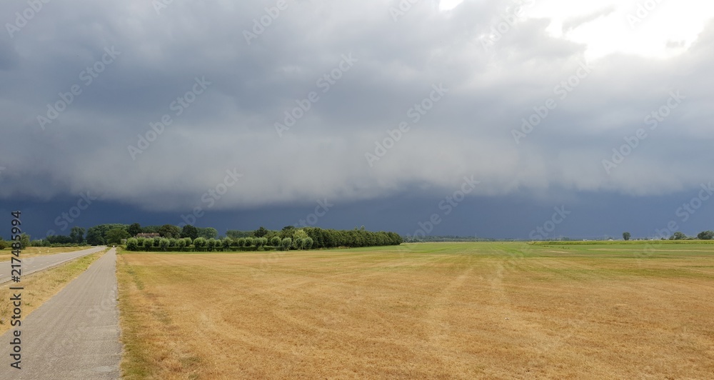 wall cloud of a thunderstorm above dry yellow fields and green trees in Laag Zuthem in Overijssel, the Netherlands