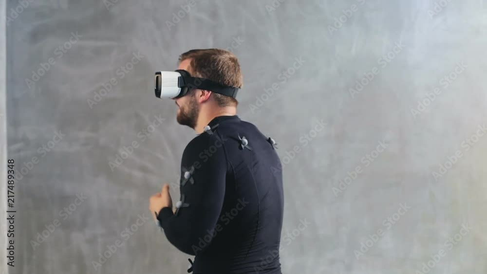 portrait of cheerful young man have fun dance while getting experience using 3D VR headset glasses of virtual reality in grey studio motion capture system suit with sensors developers testing program portrait of cheerful young man have fun dance while getting experience using 3D VR headset glasses of virtual reality in grey studio motion capture system suit with sensors developers testing program