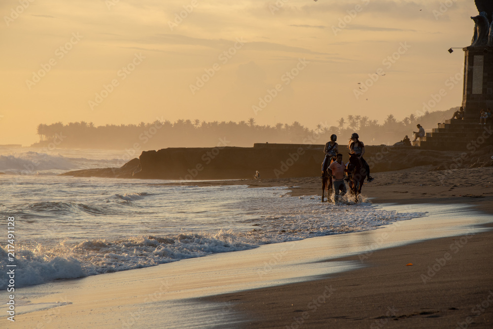 group of people having horse riding adventure on sand sea beach with sunset in the background. Active people and outdoor activity on tropical summer vacations. Chenggu Echo beach. Bali Indonesia