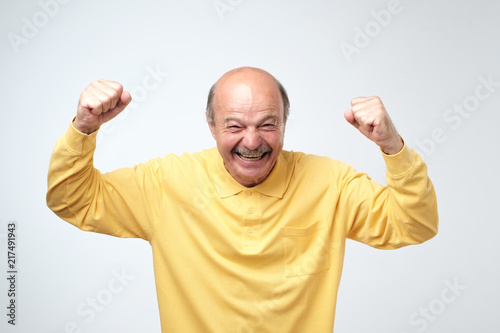 mature hispanic man in yellow shirt celebrating victory of his team over gray background.
