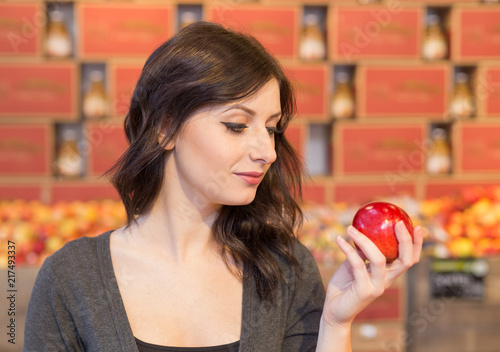 Girl in grocery store holding a red apple while smiling.