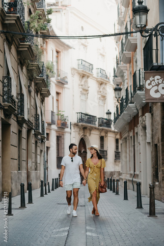 Stylish brunette girl in the hat with her boyfriend with beard walking together in the center of the old European street in Spain on the sunset