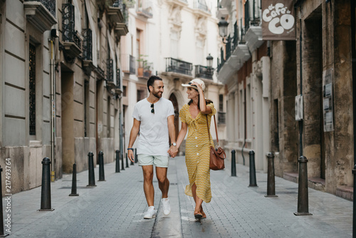 Stylish brunette girl in the hat with her boyfriend with beard walking together in the center of the old European street in Spain in the evening  photo
