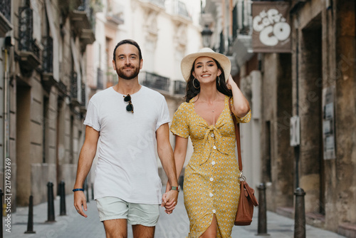 Obraz na płótnie Stylish brunette girl in the hat with her boyfriend with beard walking together in the center of the old European street in Spain in the evening. Close portrait w salonie