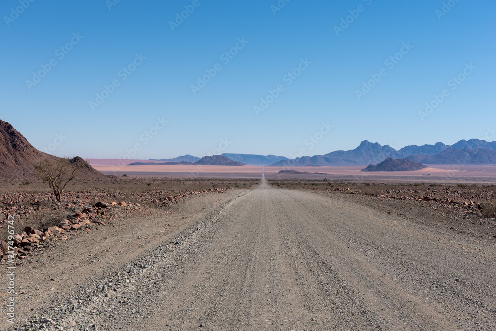 Straight empty gravel road into the distant with beautiful mountains in the background
