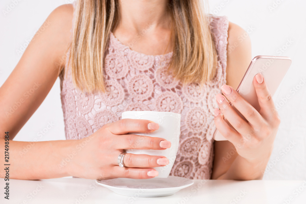 Beautiful young female with cup on coffee in hand and smart mobile phone with lace cream color dress. Fashion and beauty concept. Close up, selective focus Beautiful young female with cup on coffee in hand and smart mobile phone with lace cream color dress. Fashion and beauty concept. Close up, selective focus