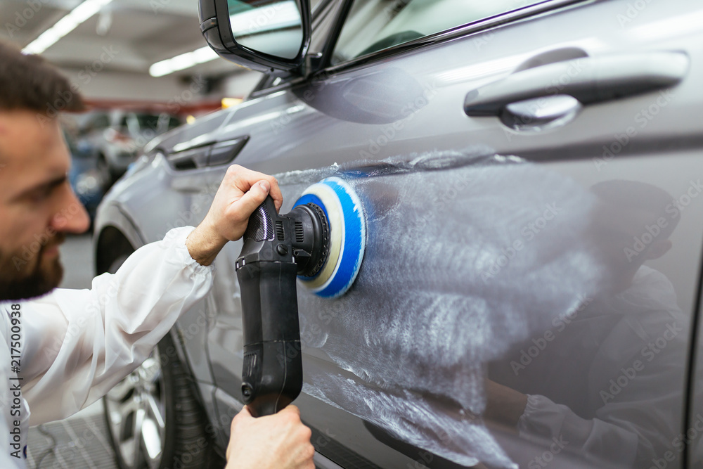 Car detailing - Worker with orbital polisher in auto repair shop. Selective focus. Car detailing - Worker with orbital polisher in auto repair shop. Selective focus.