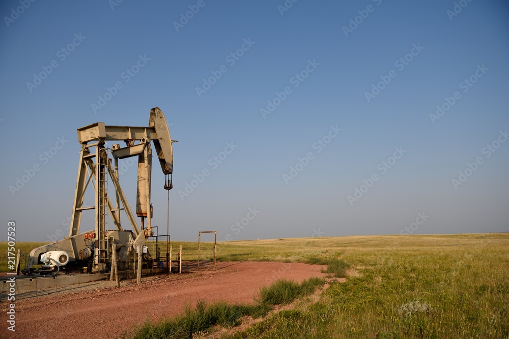 Crude oil pump jack with rural fields and clear blue sky at sunset in Wyoming, with Copy Space. Crude oil pump jack with rural fields and clear blue sky at sunset in Wyoming, with Copy Space.