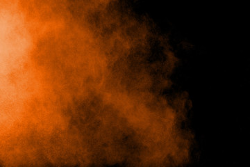 Abstract orange powder explosion on black  background. Freeze motion of orange  dust particles splash.