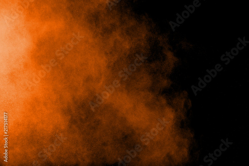 Abstract orange powder explosion on black  background. Freeze motion of orange  dust particles splash.
