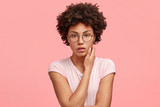 Photo of serious female freelancer in casual outfit, looks mysteriously at camera, keeps hand on neck, contemplates about new strategy in work, poses against pink background. People and lifestyle