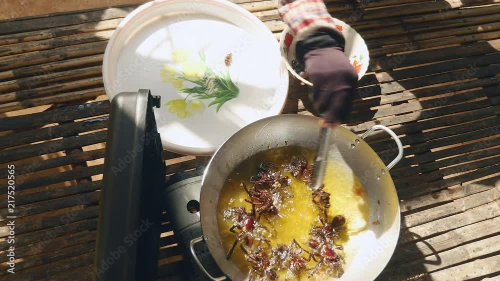 Woman taking deep fried tarantulas out of a wok using metal tongs and putting them into a plate (upper view)