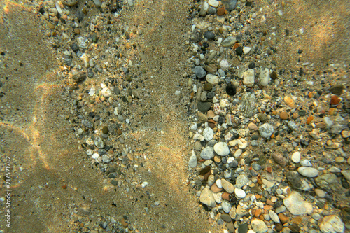 Underwater photo - sand sea bottom with small pebbles and stones, lit by sun, shot from above. Abstract marine background. © Lubo Ivanko