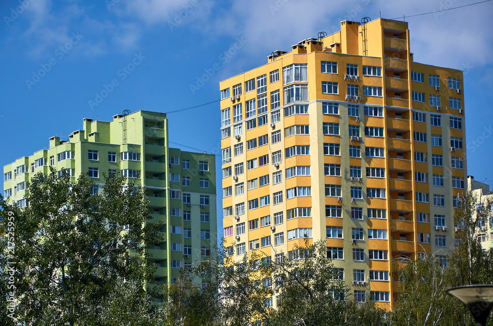 New colored apartment houses, clear blue sky, green trees in bottom