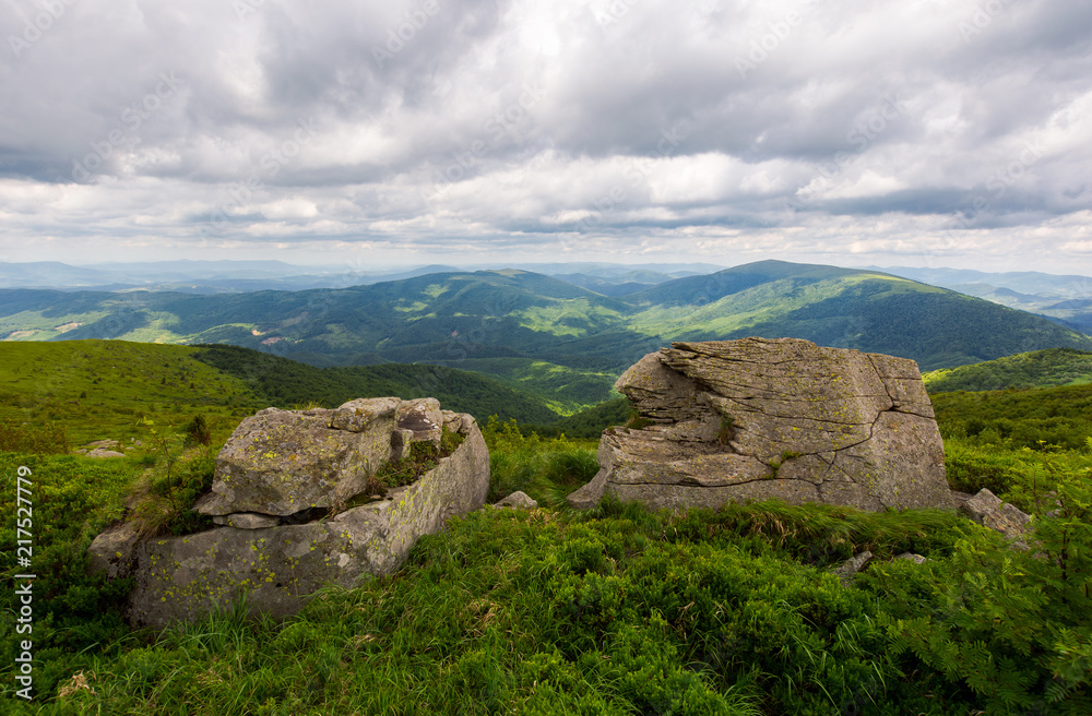 two boulders on the grassy hill. mountain range in the distance. overcast sky in summer