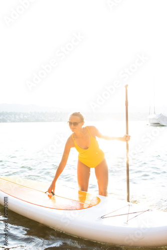 SUP Stand up paddle board concept - Pretty, young woman paddle boarding on a lovely lake in warm late afternoon light