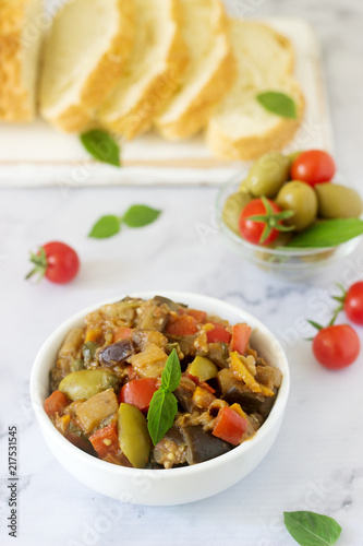 Caponata or ratatouille from a variety of vegetables served with ciabatta and olive.