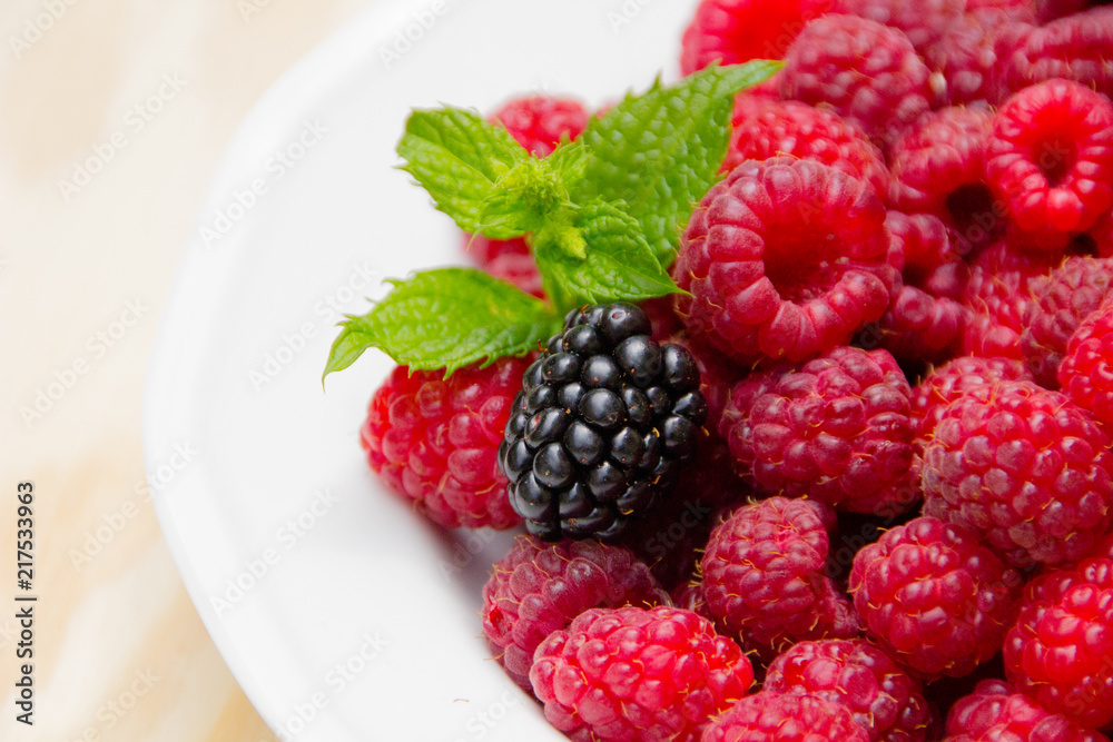 Red and delicious raspberries with mint in a white bowl Red and delicious raspberries with mint in a white bowl