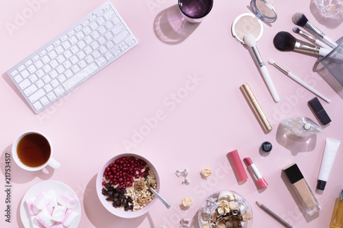 Flat lay with cup of tea or coffee, laptop or computer, woman make up products on pink background, view from above.