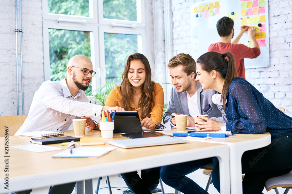 Creative workers sitting at table looking at tablet together and brainstorming. Group of university students studying together Creative workers sitting at table looking at tablet together and brainstorming. Group of university students studying together