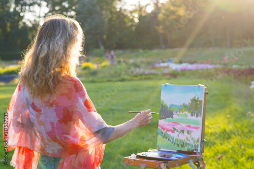 The painter paints oil paintings in the garden at sunset